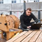 Un technicien travaille avec un ordinateur portable à côté d'une mallette énergie beige de B&W International sur un chantier - solution mobile pour l'alimentation en électricité et en données sur le terrain.