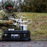 Schwarzer Energy Case von B&W International im Concamo-Tarnmuster, geöffnet mit Drohne – militärischer Outdoor-Einsatz in Tarnumgebung.