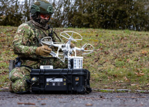 Schwarzer Energy Case von B&W International im Concamo-Tarnmuster, geöffnet mit Drohne – militärischer Outdoor-Einsatz in Tarnumgebung.